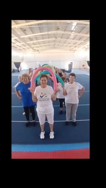 Aula de ginástica sénior no pavilhão, participantes a segurar arcos coloridos