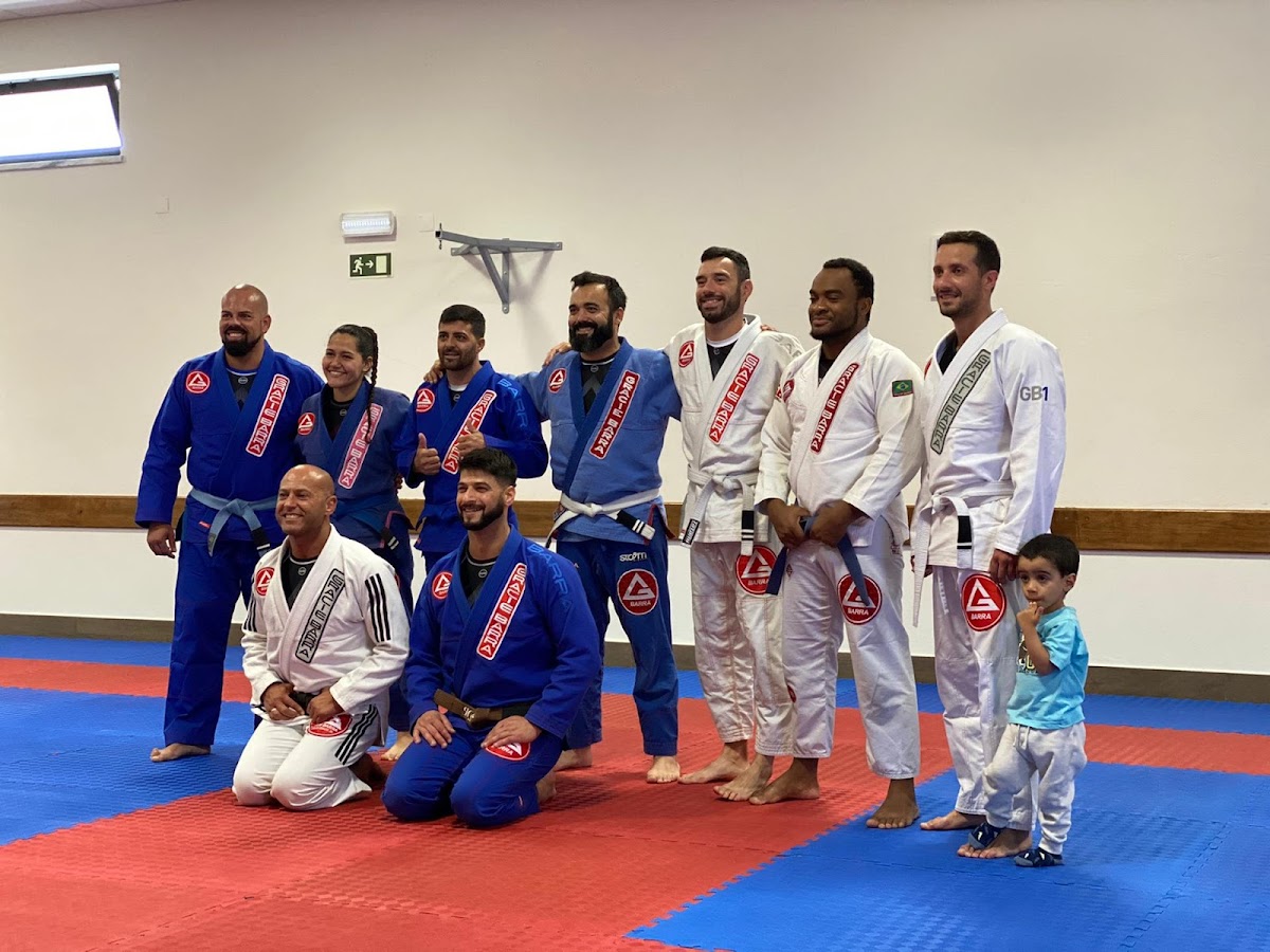 Grupo de jiu-jitsu (Gracie Barra) no pavilhão, adultos de quimono azul e branco sobre os tatamis vermelhos e azuis